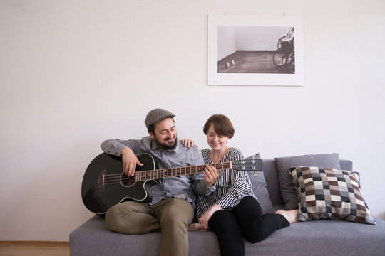 A young man is rehearsing on a bass guitar while the girlfriend is admiring him