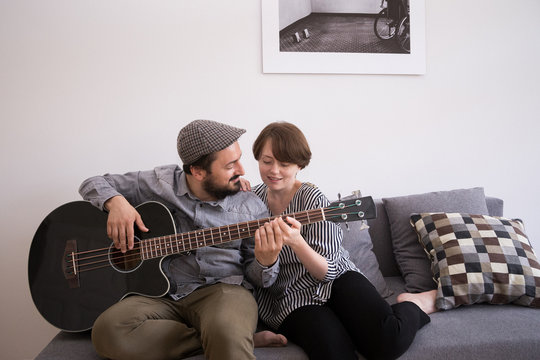 A young man is rehearsing on a bass guitar while the girlfriend is admiring him