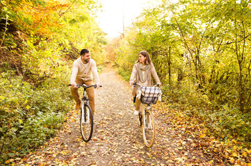 Young couple in warm clothes cycling in autumn park.