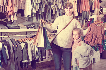 Pregnant mother and daughter choosing romper suit for baby in children’s clothes shop