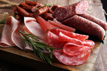 Marble cutting board with prosciutto, bacon, salami and sausages on wooden background. Meat platter