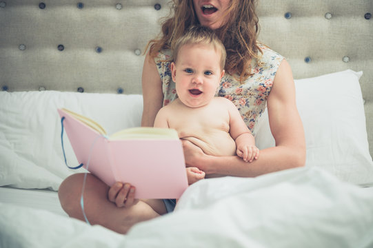 Young mother in bed reading to her little baby