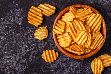 Crispy potato chips in a bowl on stone background.