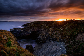 Fototapeta premium The glowing Eye: Far in the distance the Sun came staring at the Land from just under the Clouds layer in Portrane, County Dublin, Ireland