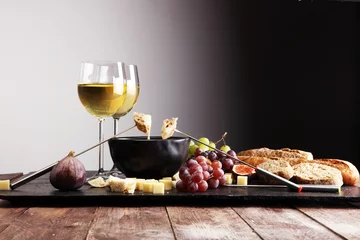 Foto op Aluminium Gourmet Swiss fondue dinner on a winter evening with assorted cheeses on a board alongside a heated pot of cheese fondue with two forks dipping bread and white wine behind in a tavern or restaurant © beats_