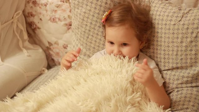 Charming charming baby goes to bed on the bed and takes cover with a white blanket. Joy and happiness of childhood. Healthy sleep.
