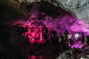 Beautiful underground cave with stalactites and stalagmites in violet illumination