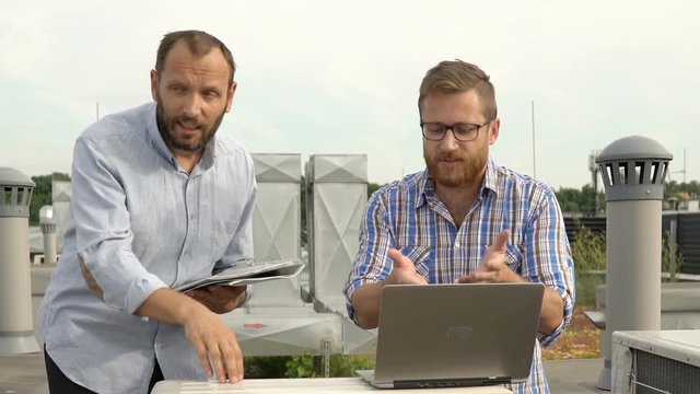 Men standing on the roof and quarrelling about air condition, steadycam shot
