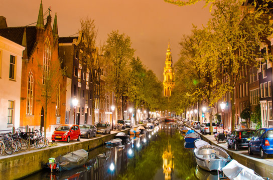 Magic night landscape in Amsterdam, Netherlands, Europe with boats on the canal and the church spire