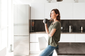 Fototapeta premium Widok z boku uśmiechnięta dorywczo kobieta pije kawę w kuchni