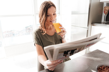 Casual woman drinking juice by the table on kitchen