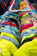 Variety of winter clothes on metal hangers. Colorful winter jackets hanging on hangers on a rack in a store