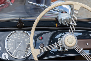 Obraz premium Kutna Hora, Czech Republic - August 18, 2017: Closeup of a blue dashboard, with speedometer and steering wheel, of a vintage car parked in the historic city center