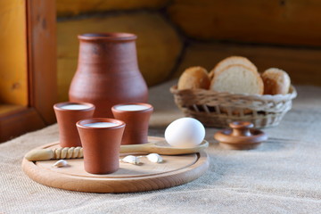 Cups with milk and a wicker basket with bread. Clay cups with milk and a wicker basket with bread are on the table near the window in the village house.