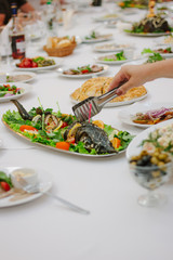 Hand with tongs keeping pieces of fish during banquet.
