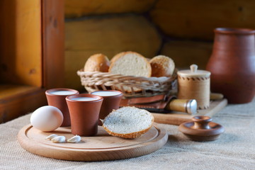 Cups with milk and a wicker basket with bread. Clay cups with milk and a wicker basket with bread are on the table near the window in the village house.