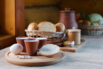 Cups with milk and a wicker basket with bread. Clay cups with milk and a wicker basket with bread are on the table near the window in the village house.