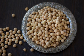 Soybeans in metal plate over black wooden background.
