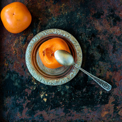 Persimmon ready to eat on silver plate and spoon.