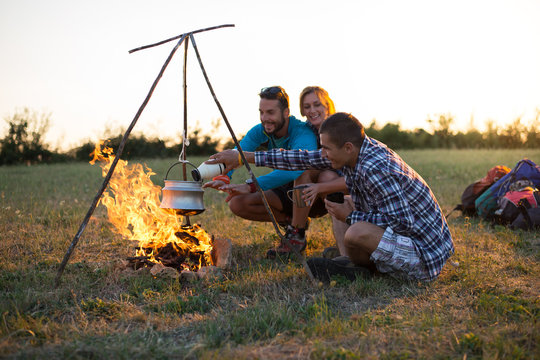 Friends camping at sunset with kettle
