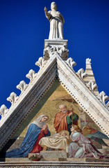 Figur und Gemälde auf dem Dreiecksgiebel der Westfront des Doms von Sienna vor strahlend blauem Himmel
