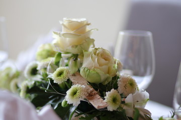 Blumengesteck mit Rosen und Chrysanthemen auf einem festlich gedeckten Tisch