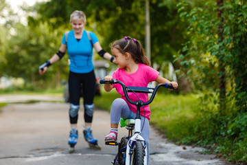 Naklejka premium mother goes on rollers. Daughter riding a bicycle