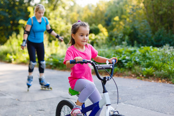 A young mother roller skating. her Daughter riding a bicycle