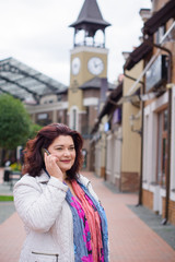 Fototapeta premium Mature cheerful woman talking on a mobile phone in the city and walking among the old part of the city. Good news and good mood
