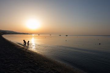 Close-up of little girls playing in the sea water at sunrise. Children's silhouette playing in golden hour.