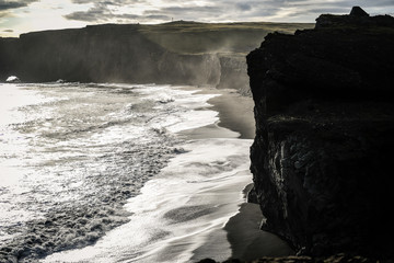 View of the cliff on the black beach of Iceland with waves and huge black rocks.