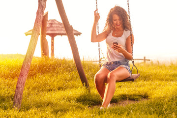 Young woman on a swing on a sunny autumn day. She is looking at smart phone.