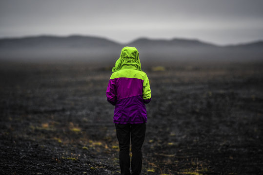 Woman looking on a Iceland landscape, black volcanic dust and mountains with fog in background.