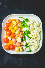 Raw vegetables in a baking dish- tomatoes, cauliflower, zecchini, potato. Ready for roasting. top view, space for text.
