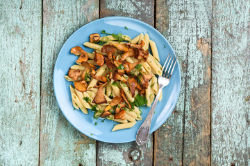 Vegan penne pasta with forest chanterelle mushrooms in turquoise plate on old wooden table copyspace