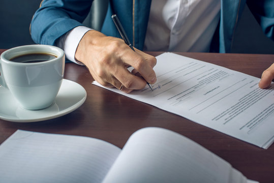 Businessman Signs Important Legal Documents On The Desktop With Cup Of Coffee