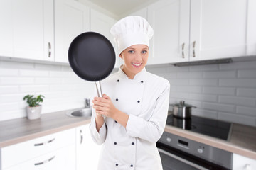 happy young woman in chef uniform with frying pan in modern kitchen