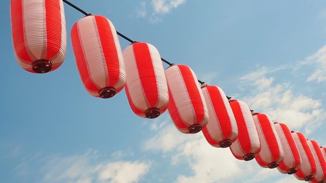 Paper red-white japanese lanterns Chochin hanging on blue sky background.