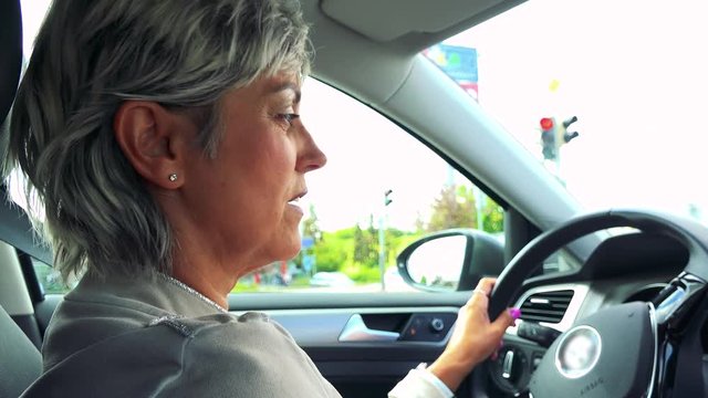 Middle aged woman drives a car, waits on the traffic lights in the city 