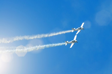 Light engine airplane with a trace of white smoke fly in groups in the blue sky with sunlight and glare