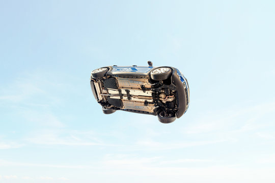 A car flying through the air (in the pale blue sky) with the underside including, wheels, engine and exhaust pipe visible.