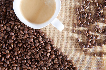 Cup of coffee on a background of coffee beans and a jute bag. 