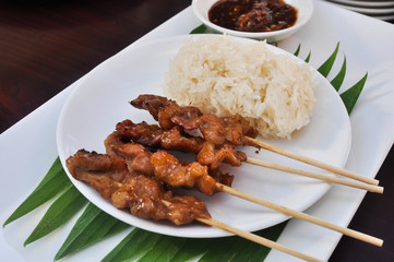 Close-up of grilled pork with sweet spicy sauce and sticky rice on plate: Thai street food.