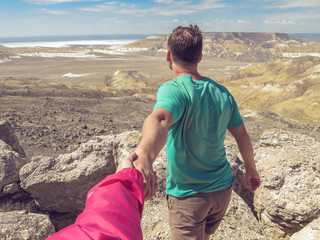 Hiker young man holding woman's hand and leading him on nature outdoor. Couple in love. Desert