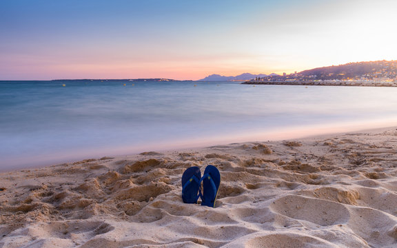 Flip flops on a sandy beach at sunset