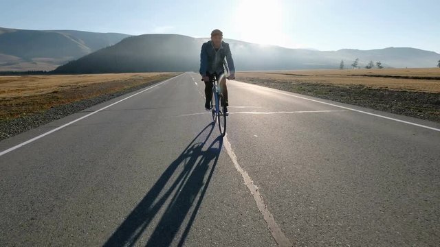 Young handsome man riding at vintage bicycle in the country road. Sporty guy cycling at the track. Male cyclist riding fixed gear bike at highway. Healthy active lifestyle 20s 4k.