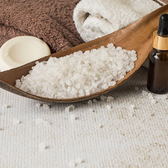 
 Beauty and hygiene. Body care. Sea salt, a bottle of essential oil, a round piece of soap and terry towels on a light background.
