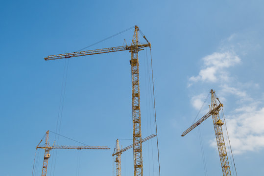 Yellow tower cranes against blue sky