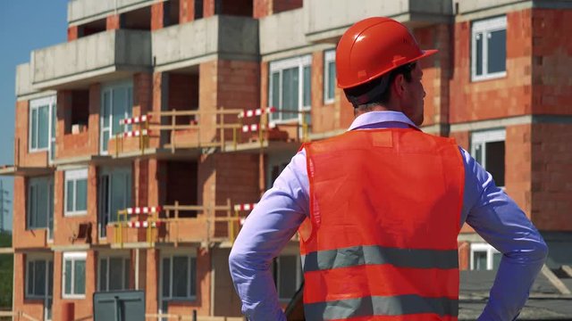 Construction worker looks around and thinks in front of building site - shot on back