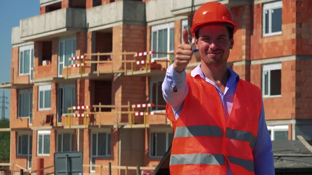 Construction worker shows thumb up and agrees in front of building site